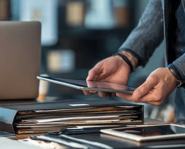 Professional person using a digital tablet above a desk with document folders and a laptop.