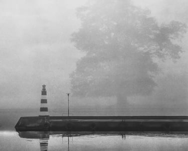 A foggy day captures a black and white lighthouse, emphasizing its silhouette against the misty background.