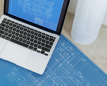 Open laptop with blueprints on the screen sitting on top of printed out blueprints