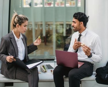 2 people in business meeting while eating sandwich outside with laptop