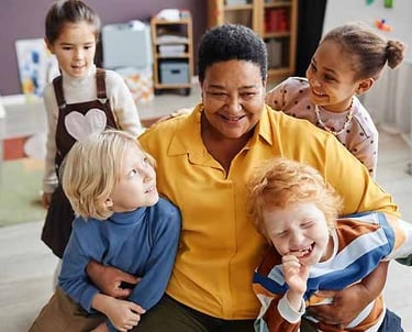 A happy childcare staff member plays with children at their childcare centre