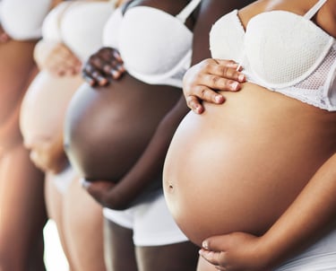 Diverse group of pregnant women standing in a row cradling their bellies.
