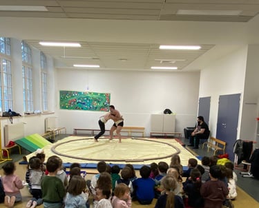 Des enfants regardent 2 hommes lutter sur un dohyo