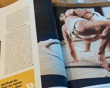 Photo d'un magazine avec sur la page de droite 2 hommes en mawashi, dont l'un a la main au sol suite a une clé de bras