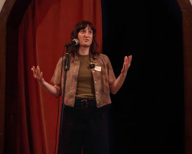 Young confident woman behind microphone speaking to audience using hand gestures