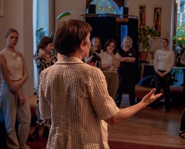 Female public speaking trainer behind microphone, talking to women during workshop.