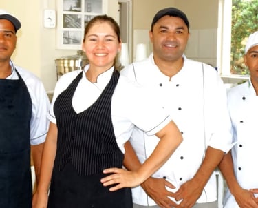 A smiling restaurant kitchen staff and servers posing in professional uniforms and chef hats.