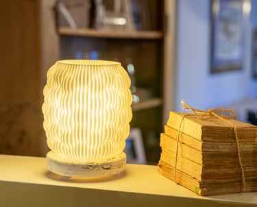 A warm, 3D printed textured lamp glowing next to a stack of vintage books on a shelf.