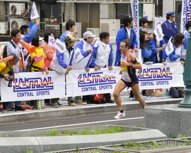 Coach Scott Brown running the Osaka marathon with a crowd of people cheering him on.