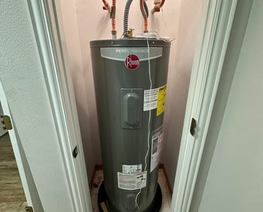 Rheem Performance electric water heater installed in a residential utility closet with copper piping.