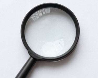 Hand holding a magnifying glass over a document for close-up reading and inspection.