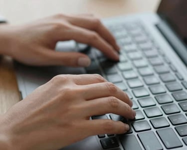 A detailed shot of a person's hands typing on a laptop keyboard in a bright office environment, symbolizing the creation of effective vacancy texts.