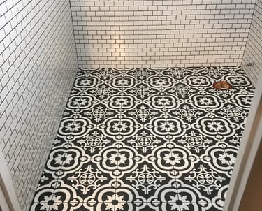 Black and white patterned floor tile installed in a half bathroom with white subway tile walls.