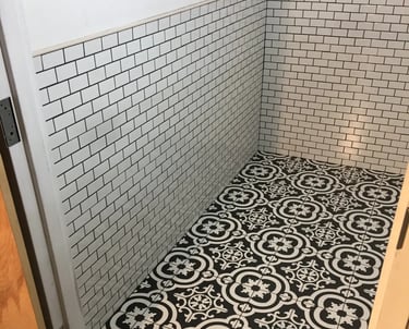 Black and white patterned floor tile installed in a half bathroom with white subway tile walls.