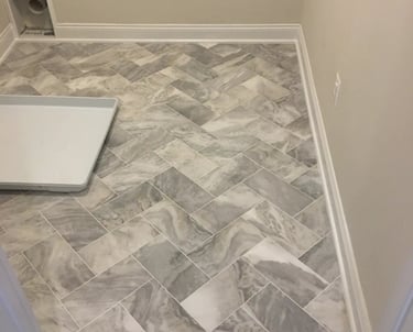 Gray marble-look porcelain tile installed in a herringbone pattern in a laundry room.