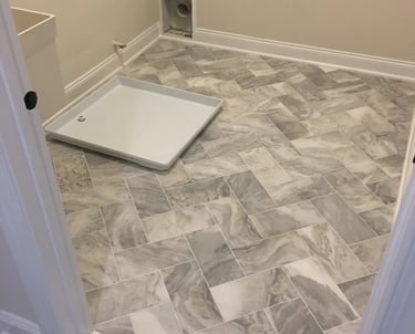 Gray marble-look porcelain tile installed in a herringbone pattern in a laundry room.