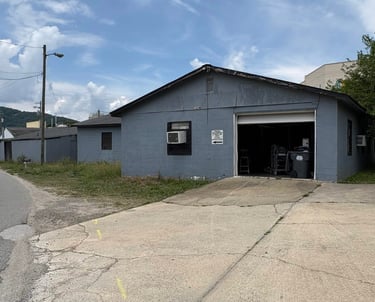 Gray concrete block industrial building with an open garage bay and adjacent driveway.