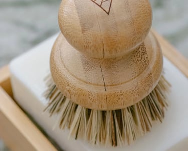 A wooden handled pot scrubber placed on a bar of white soap