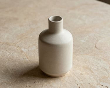 A minimalist ceramic vase on a warm sand colored stone table. No plants or flowers. Geometric and serene.