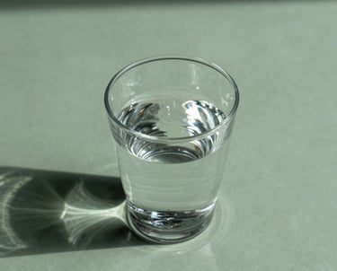 Abstract shot of a glass of water on a sage green surface, with sunlight creating ripples and shadows. Calm and refreshing. No people.