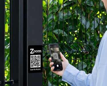 A person scans a Zoomm QR code on a black metal gate with a smartphone for secure entry access.