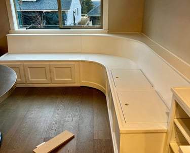 Custom white built-in window seat with storage and curved corner bench seating in a home.