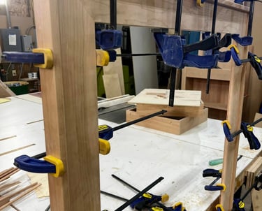 Wooden cabinet door frame being glued and secured with blue Irwin quick-grip clamps in a workshop.