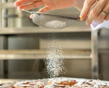 Un chef pastelero espolvoreando azúcar glass sobre tartaletas recién horneadas
