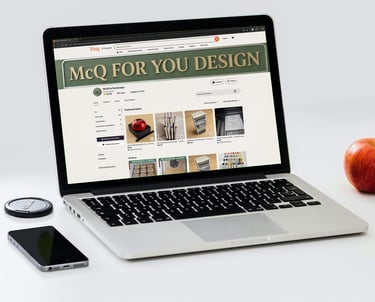 A silver laptop displaying the MCQ For You Design Etsy shop page next to a red apple and smartphone.