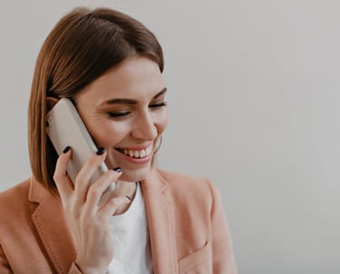 Smiling professional woman in a peach blazer talking on a smartphone during a business call.