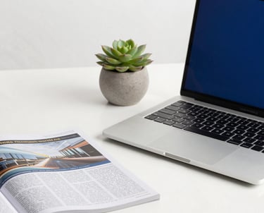 A minimalist workplace with a high-end laptop, financial magazines, and a succulent. Oxford blue and gold color accents. Professional photography.