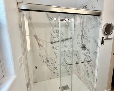 Modern walk-in shower with white marble wall tiles, sliding glass doors, and ADA compliant grab bars.
