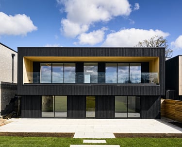 Modern two-story black timber-clad house featuring glass balconies and large windows.