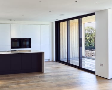 Modern minimalist kitchen with a black island, white cabinets, and large sliding glass doors.