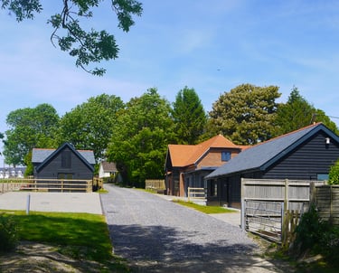 Modern black timber barn conversion cottages along a gravel driveway in a rural countryside setting.