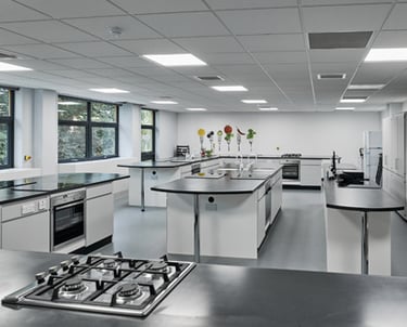 Modern teaching kitchen with stainless steel appliances and black countertops.