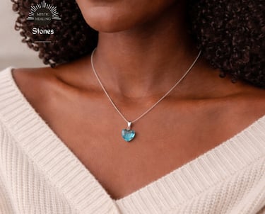 A woman wearing a silver chain necklace with an aquamarine heart-shaped crystal pendant.