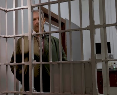 Famous Actor Jack Mulcahey stands looking in through the bars of a jail cell. From "60 Miles North"