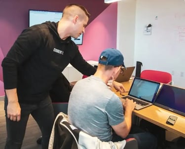 Two individuals collaborating in a modern tech workspace with laptops, screen, and whiteboard for UI planning.