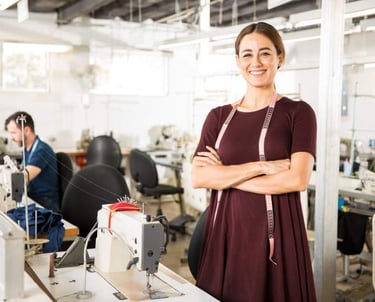 Una diseñadora de moda sonriente, con una cinta métrica en la mano, se encuentra en una fábrica