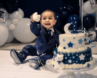 a baby boy in a suit and tie, sitting next to a birthday cake