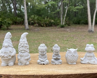 Collection of tiny stone garden figurines including gnomes, meditating Buddhas, an owl, and a frog.