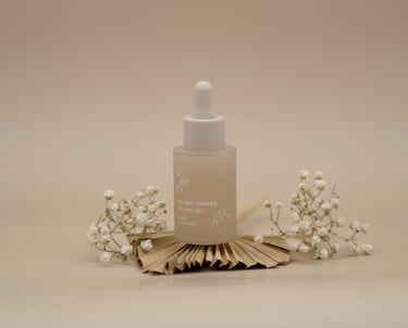 Sticluță de esență calmantă, cu pipetă albă, așezată central pe fundal bej, decorată cu flori albe delicate