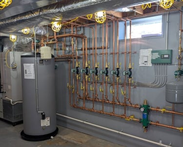 Professional basement boiler installation with copper piping, circulator pumps, and water storage tank.