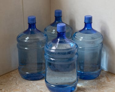 Office worker struggling with heavy water garrafas stacked in a cluttered storage room.