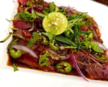 Aguachile de atún fresco con cebolla morada, jalapeños, lima y cilantro en un plato blanco.