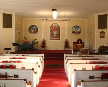 Interior view of a traditional church sanctuary with white pews, red carpet, stained glass windows, and a central altar.