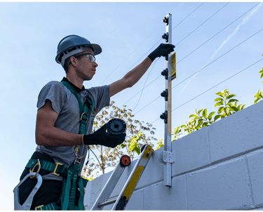 Professional technician installing an electric security fence on a white perimeter wall.