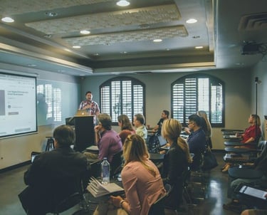 Un profesor presenta un taller de inglés a un grupo diverso de personas en un salon de clases.