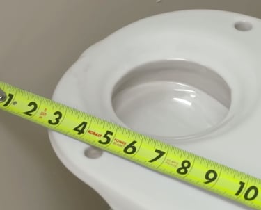 Measuring a white toilet flange using a yellow Kobalt tape measure for bathroom plumbing repair.